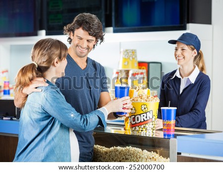 Happy expectant couple buying snacks from female seller at cinema concession stand