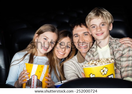 Portrait of happy family of four with popcorn at cinema theater