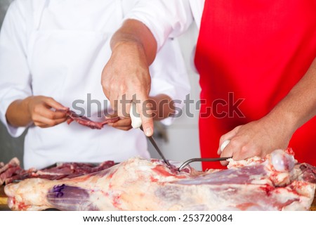 Midsection of butcher cutting meat by colleague at counter in butchery