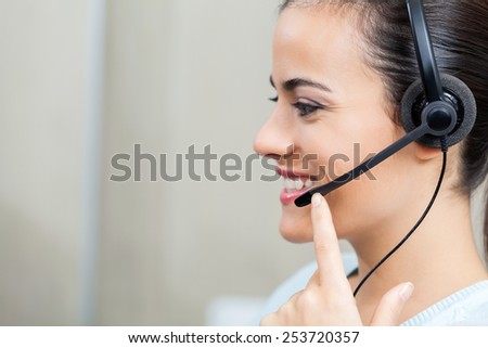 Side view of happy female customer service representative using headset at office