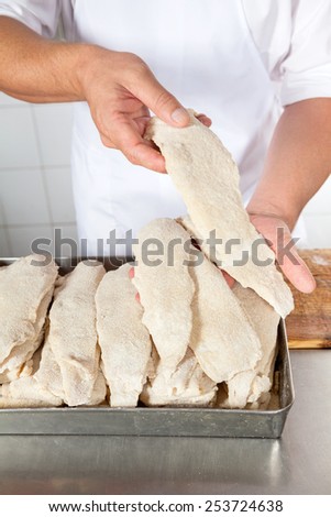 Midsection of male butcher holding chicken pieces covered with flour in shop