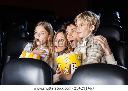 Shocked family of four with popcorn watching movie in cinema theater