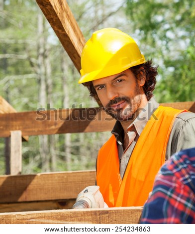Portrait of confident male worker drilling on timber frame at construction site