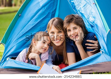 Portrait of happy children with mother holding book in tent at park