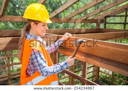 Side view of smiling female construction worker hammering nail on timber frame at site