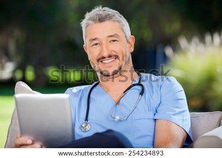 Portrait of smiling male doctor with tablet computer sitting at nursing home porch