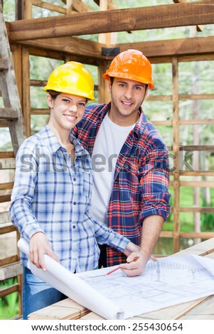 Portrait of happy male and female architects examining blueprint at construction site