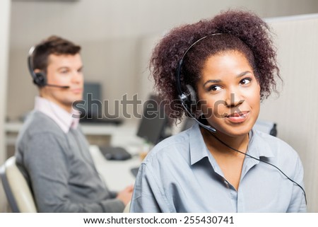 Female customer service representative wearing headset with male colleague in background at office