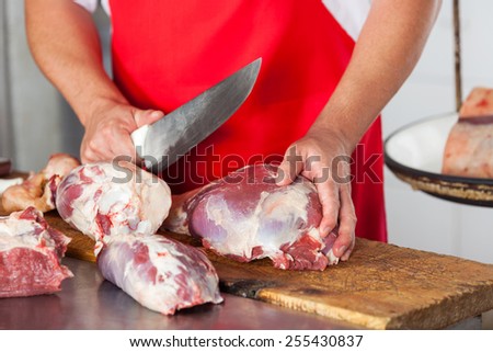 Midsection of male butcher cutting meat with knife in butchery