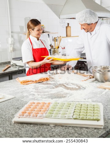Happy female chef showing pasta tray to male colleague at commercial kitchen counter