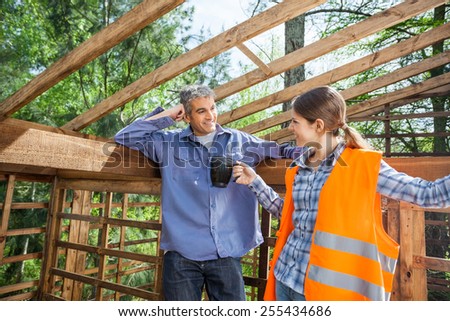 Female construction worker giving coffee mug to male colleague at site