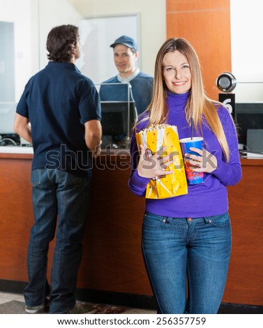 Portrait of beautiful woman holding snacks while man buying tickets at box office counter