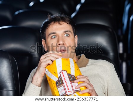 Frightened man eating popcorn while watching movie in cinema theater