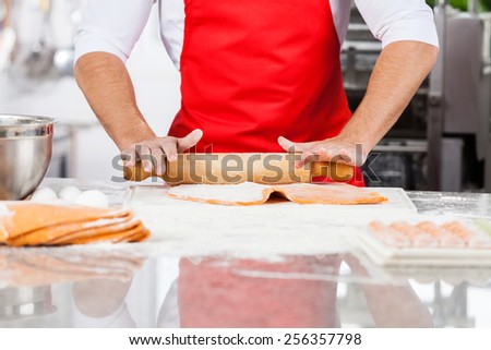 Midsection of male chef rolling ravioli pasta sheet at counter in commercial kitchen