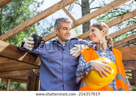 Happy female worker looking at colleague holding coffee mug at construction site