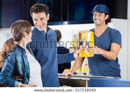 Loving expectant couple buying popcorn from male seller at concession stand in cinema