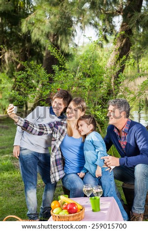 Smiling family taking selfportrait through cellphone at campsite