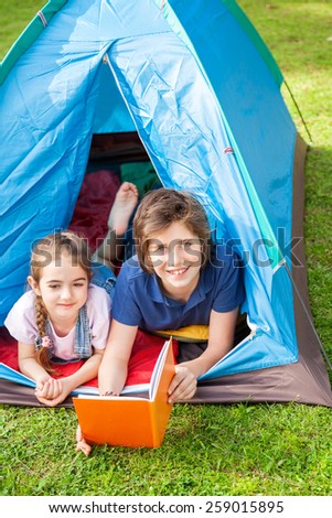 Portrait of happy boy with sister reading book in tent at park