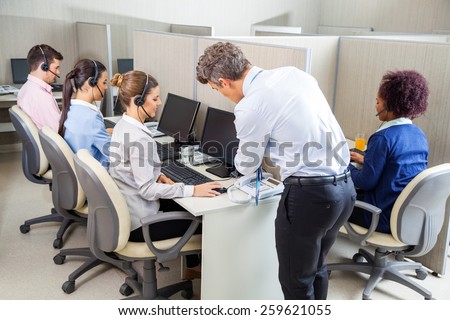 Manager assisting young female customer service agent while employees working in call center