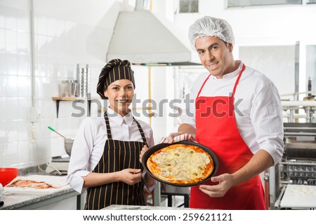 Portrait of happy male and female chefs presenting pizza in pan at commercial kitchen