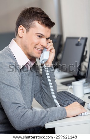 Smiling male customer service representative using landline phone at desk in office