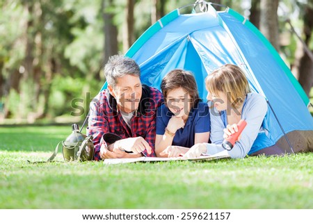 Happy family studying map while lying in tent at park