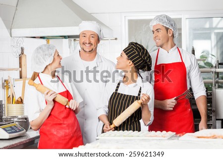 Happy chefs looking at male colleague while preparing pasta in commercial kitchen