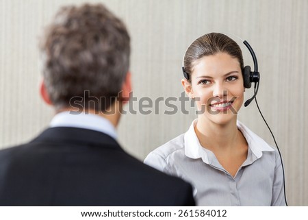 Young female customer service representative wearing headset while looking at manager