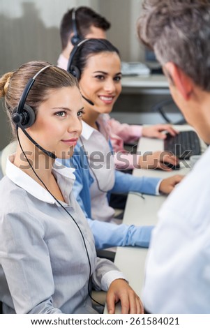 Female customer service executives looking at manager while sitting at desk in call center