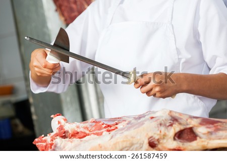 Midsection of female butcher sharpening knife to cut meat in butchery