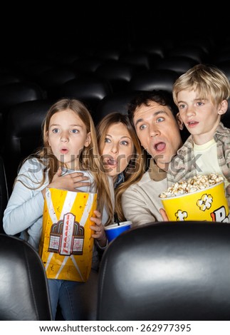 Shocked family of four with popcorn watching film in movie theater