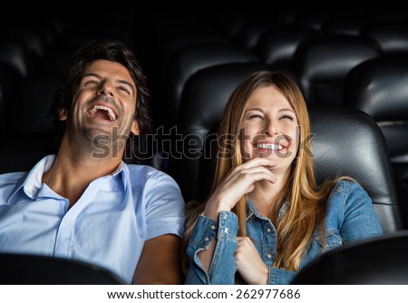 Mid adult couple laughing while watching film in movie theater