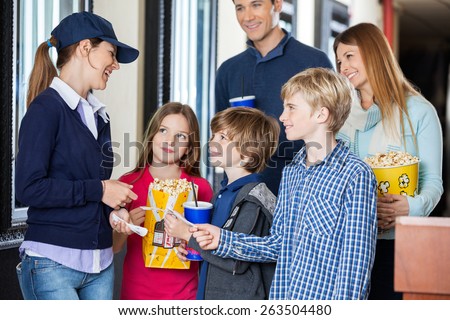 Happy young female worker checking movie tickets of family at cinema