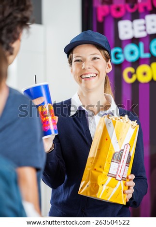 Happy female worker selling popcorn and cold drink to man at cinema concession stand