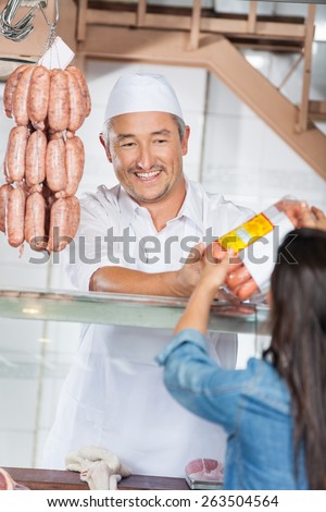 Happy mature man giving packed sausages to female customer in butcher shop