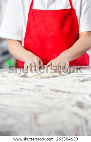 Midsection of chef kneading dough at messy counter in commercial kitchen