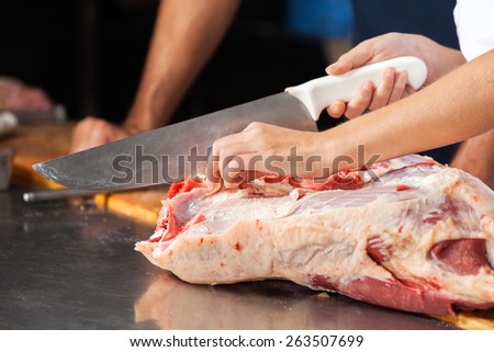 Cropped image of butcher cutting raw meat with knife in shop