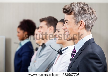 Side view of happy manager standing in row with call center employees at office