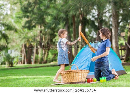 Happy siblings fighting with bread loafs by tent in park