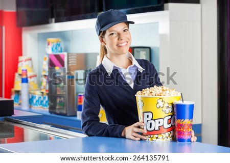 Portrait of confident female worker with popcorn and drink standing at concession stand in cinema