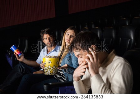 Angry couple looking at man using mobilephone while watching film in movie theater