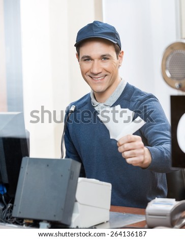 Portrait of happy male worker holding tickets at box office counter