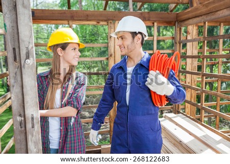 Smiling male and female construction workers in wooden cabin at site