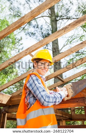 Portrait of smiling female worker cutting wood with handsaw at construction site