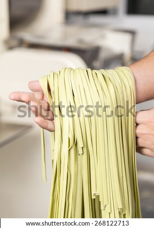 Cropped image of male chef\'s hand holding green spaghetti pasta at commercial kitchen