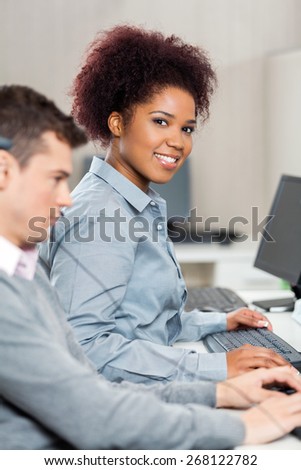 Portrait of beautiful young customer service representative with male colleague working in office