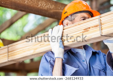 Mature male worker carrying tied wooden planks at construction site
