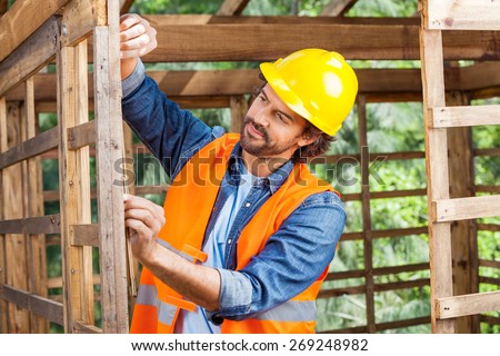 Male worker measuring timber frame with tape at construction site