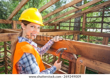Side view portrait of happy female construction worker hammering nail on timber frame at site