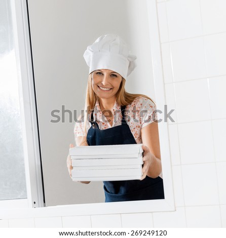 Portrait of smiling female chef holding pasta boxes at window